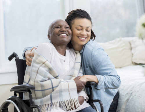 Young woman embraces her beautiful senior mother who is in a wheelchair. The adult daughter is visiting her mom in her mom's home.